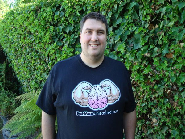 Kevin poses in a Fat Man Unleashed shirt after losing over 50 lbs.